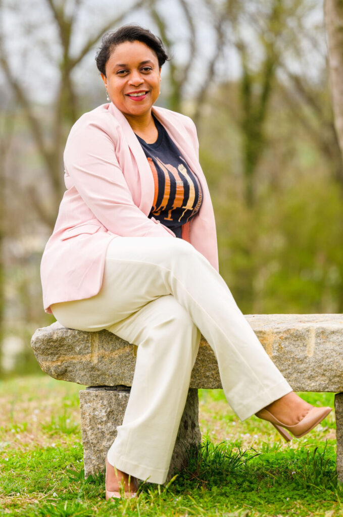 Dr. Jackson sitting on bench outside wearing a pink blazer, cream pants, and tan heels while smiling